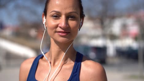 Portrait-of-sportswoman-in-earphones-smiling-at-camera-outdoor